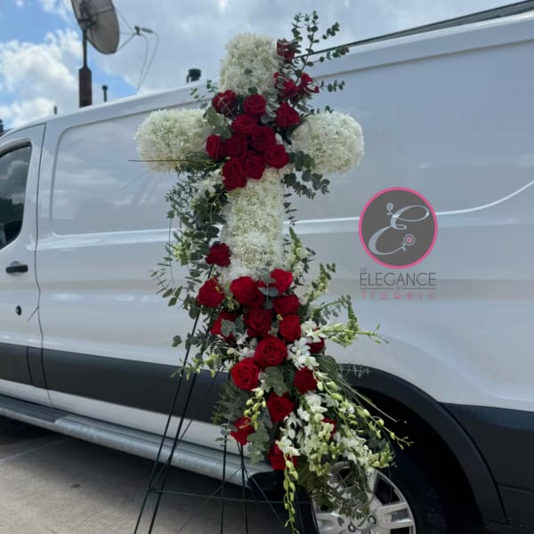 Cross-shaped floral tribute with red roses and white blooms on a stand