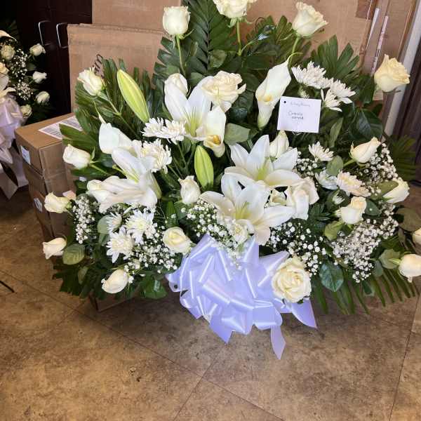 Large white sympathy arrangement with lilies and roses accented by a big white bow.