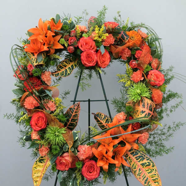 Orange and coral floral wreath on a stand with roses and lilies