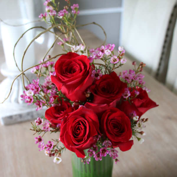 Red roses arranged in a green glass vase with small pink filler flowers
