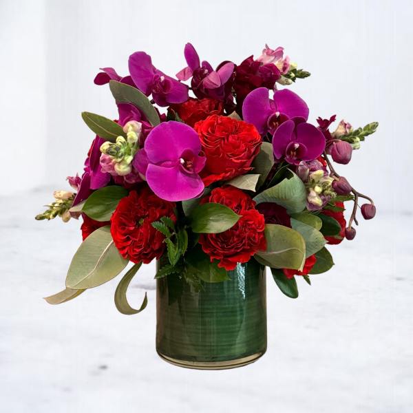 Red roses and purple orchids arranged in a green glass vase