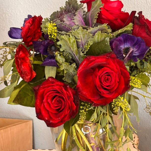 Red roses and purple anemones in a clear glass vase