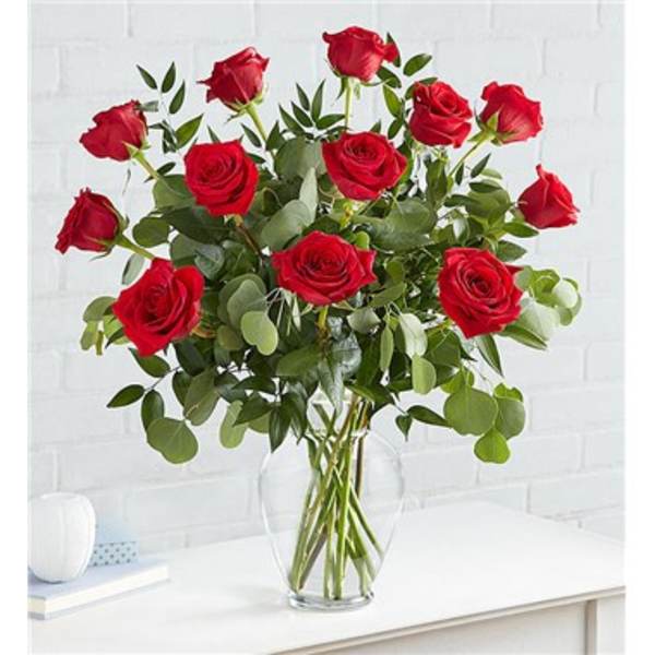 Red roses arranged in a clear glass vase with greenery