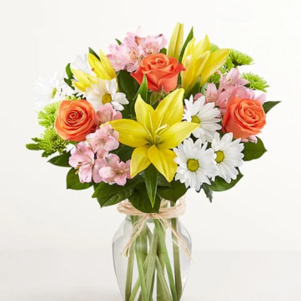 Bouquet of yellow lilies, orange roses, and white daisies in a glass vase