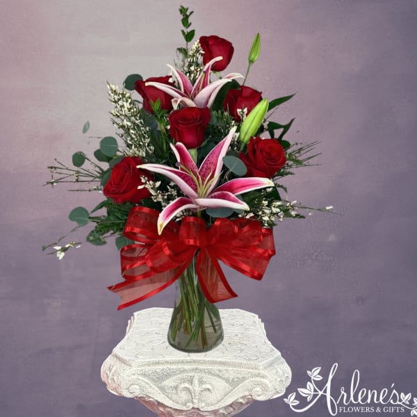 Red roses and pink lilies in a glass vase with a red bow