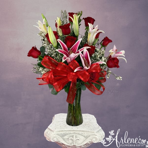 Red roses and pink lilies in a tall glass vase with a red bow