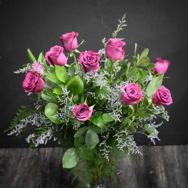 Arrangement of deep pink roses with soft lavender filler flowers in a clear glass vase