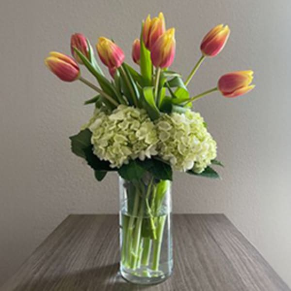 Pink tulips arranged with white hydrangeas in a clear glass vase