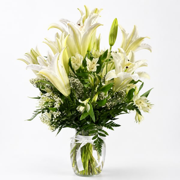 White lilies arranged in a clear glass vase with a white ribbon