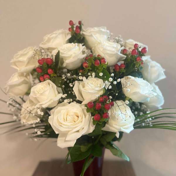 White rose bouquet with red berry accents in a dark vase