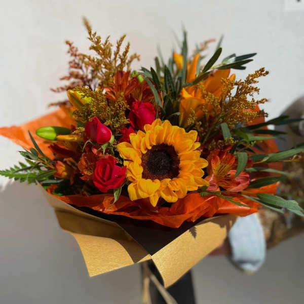 Bouquet of sunflowers and red roses wrapped in orange and gold paper