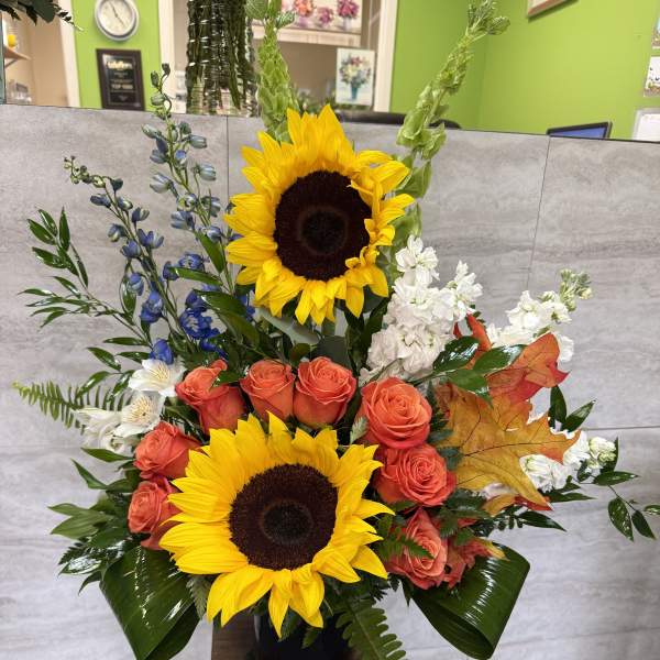 Tall floral arrangement with sunflowers, coral roses, and white blooms in a black vase