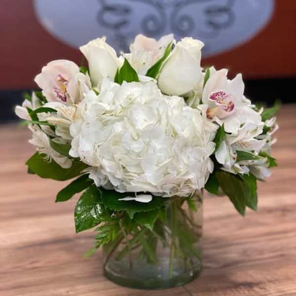 White hydrangea and pale pink orchid arrangement in a glass vase