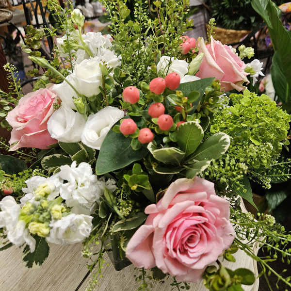 Pink roses and white blooms with berries in a lush mixed arrangement in a glass vase