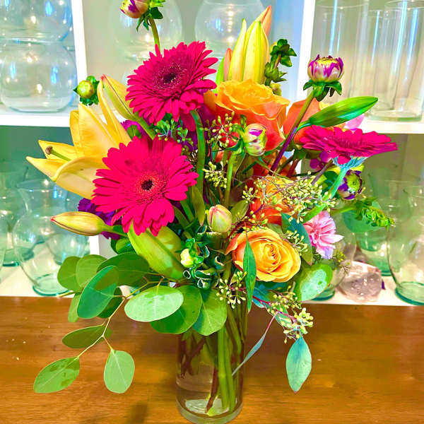 Bright mixed bouquet of gerbera daisies, roses, and lilies in a glass vase