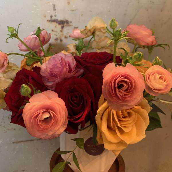 Bouquet of red, pink, and yellow roses with ranunculus in a white vase