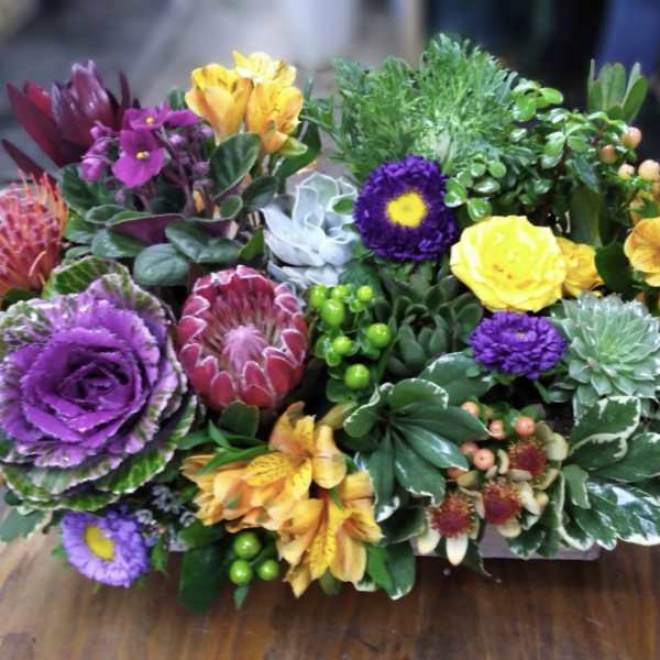 Mixed bouquet with purple, yellow, and orange flowers in a low container