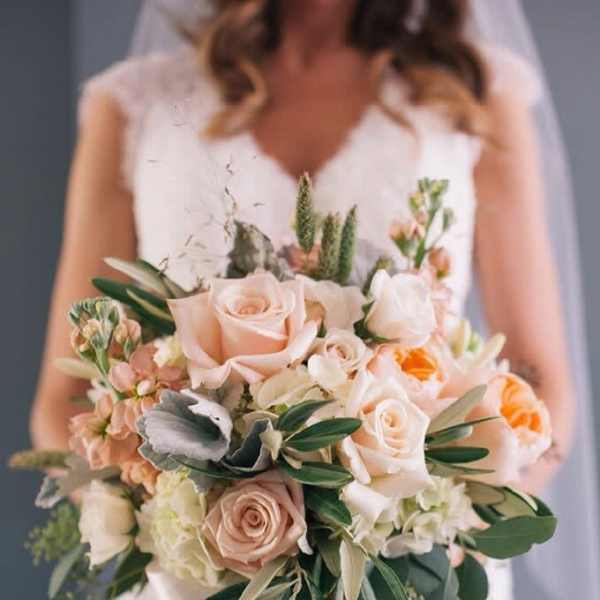 Bridal hand-tied bouquet of peach and cream roses with white blooms and ribbon wrap