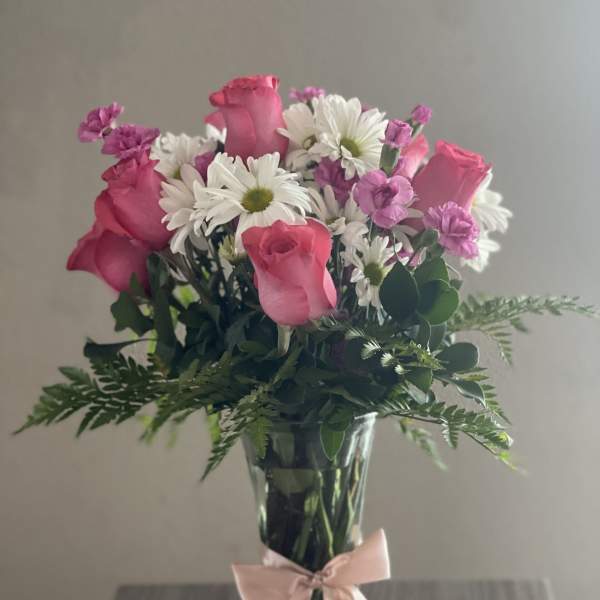 Pink roses and white daisies in a clear glass vase with a pink ribbon