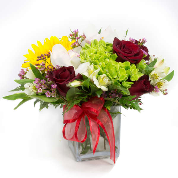 Bouquet of red roses, yellow sunflowers, and white blooms in a glass vase