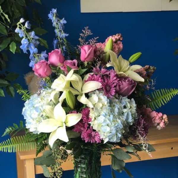 Bouquet of pink roses, lilies, hydrangeas, and blue delphinium in a glass vase