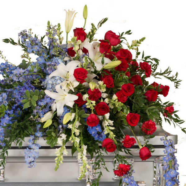 Large floral casket spray with red roses, white lilies, and blue flowers