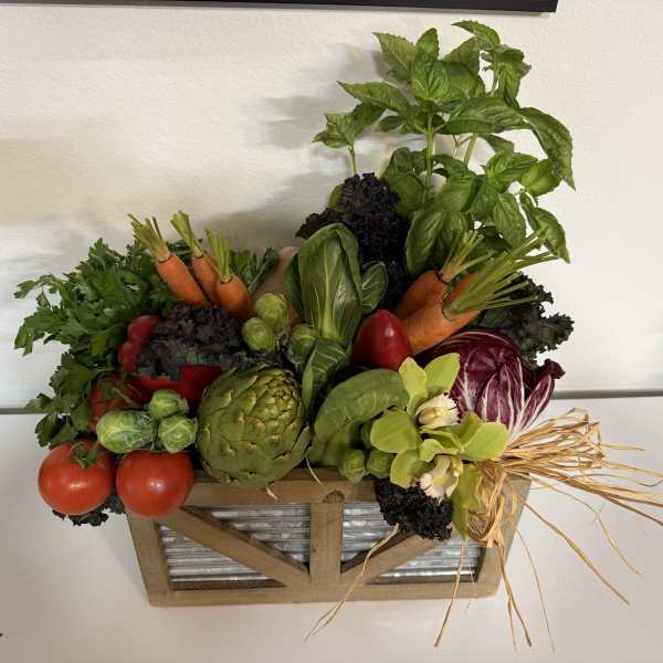 Vegetable arrangement in a wooden crate with basil, carrots, tomatoes, artichoke, and cabbage