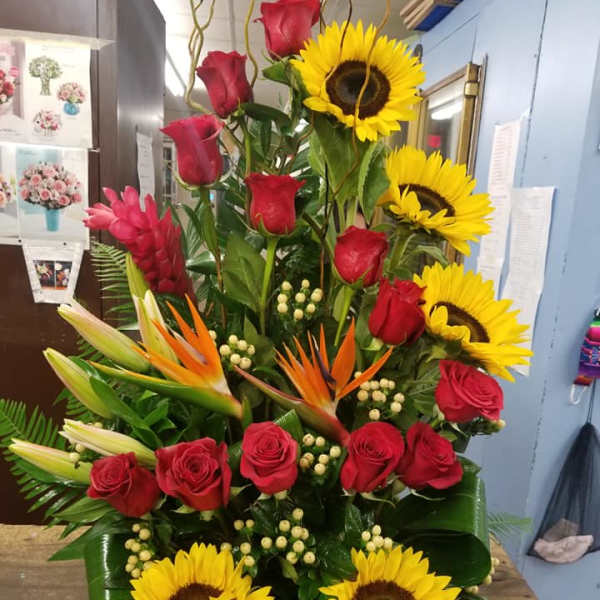 Tall arrangement of red roses, sunflowers, and tropical blooms