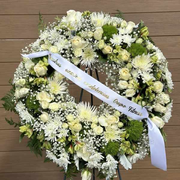 White floral wreath on an easel with a ribbon across the center
