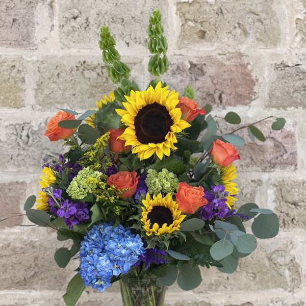 Mixed bouquet with sunflowers, orange roses, and blue hydrangea in a glass vase