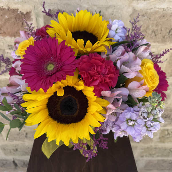 Bright mixed bouquet with sunflowers, gerbera daisies, and roses in a dark vase