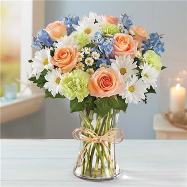 Bouquet of peach roses, white daisies, blue flowers in a glass vase