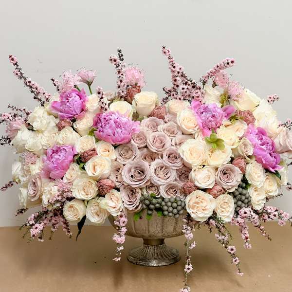 Large pastel floral arrangement in a pedestal vase with pink and cream roses