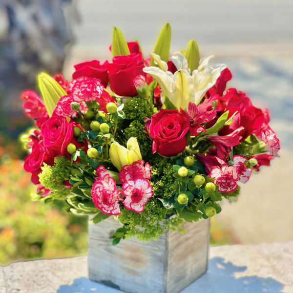 Bouquet of red roses, white lilies, and pink carnations in a square vase