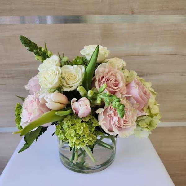 Low arrangement of pale pink roses, white roses, tulips, and green hydrangea in a clear glass vase