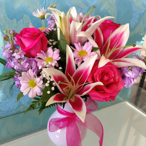 Pink roses and lilies in a white vase with a pink ribbon
