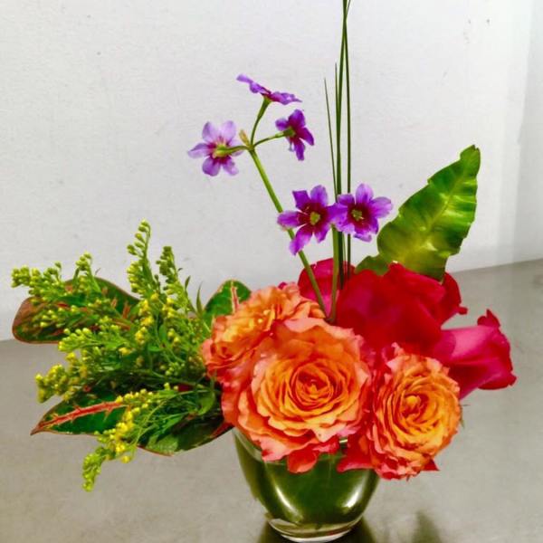 Orange roses and purple flowers in a green glass vase