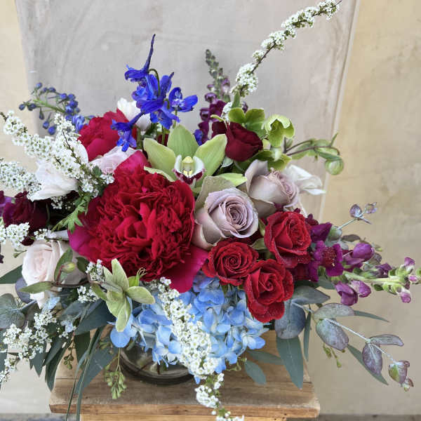 Mixed bouquet of red roses, blue hydrangea, and white filler flowers in a glass vase