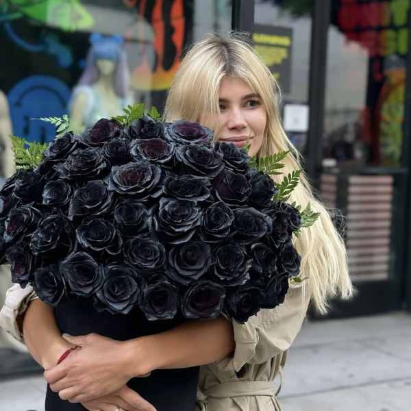 Woman holding a large bouquet of black roses with greenery