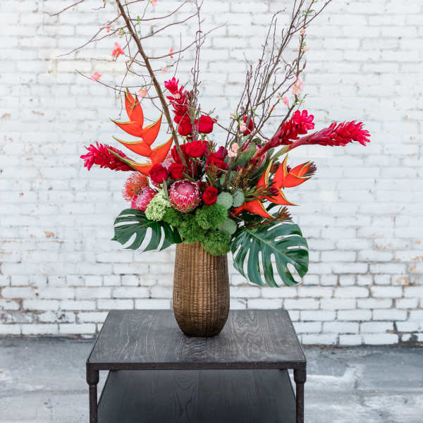 Tall tropical floral arrangement in a brown vase with red and orange blooms