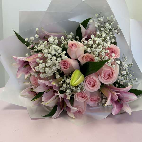 Pink roses and lilies with white baby's breath in wrapped bouquet