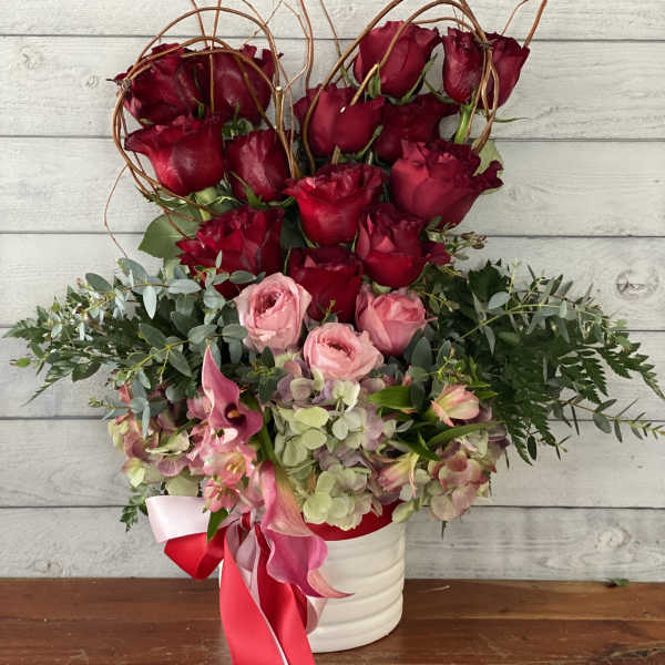 Red roses and pink flowers arranged in a white vase with ribbon