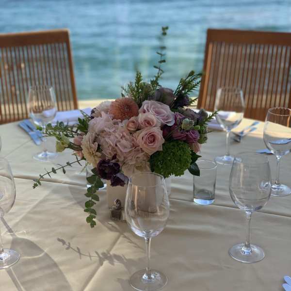 Pastel floral centerpiece in a white vase on a set dining table by the water
