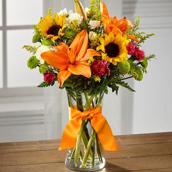 Bouquet of sunflowers and orange lilies in a glass vase with an orange ribbon