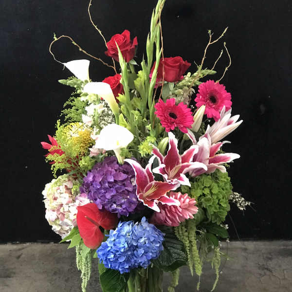 Tall mixed bouquet with roses, lilies, calla lilies, and hydrangeas in a glass vase