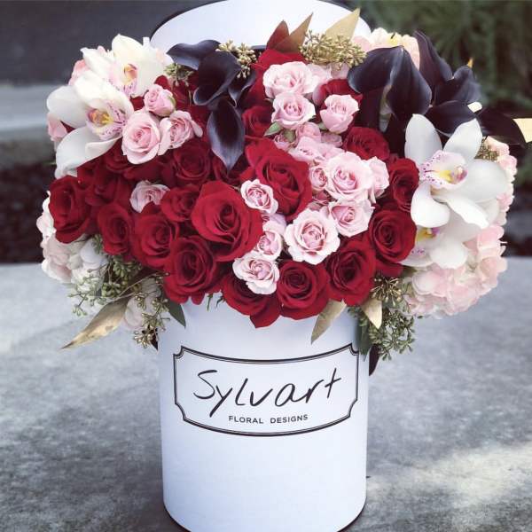 Red and pink roses with white orchids in a white hat box