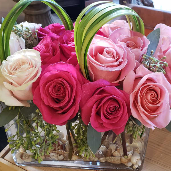Pink and white roses arranged in a clear rectangular vase