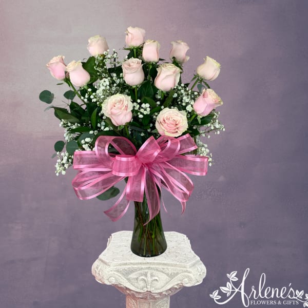 Pink roses arranged in a tall glass vase with a large pink ribbon