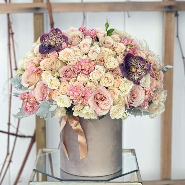 Large pastel rose arrangement in a gray hat box with purple orchids