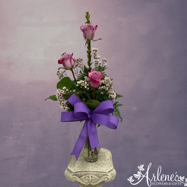 Pink roses in a glass vase with a purple ribbon